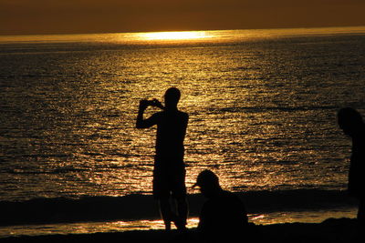 Silhouette woman standing on beach against sky during sunset