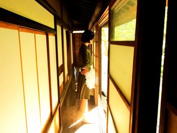 Side view of woman standing at home entrance on sunny day