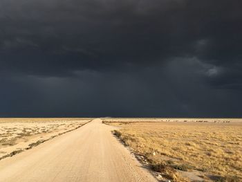 Road passing through land against storm clouds