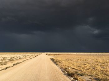 Road passing through land against storm clouds