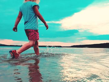 Rear view of man jumping in sea against sky