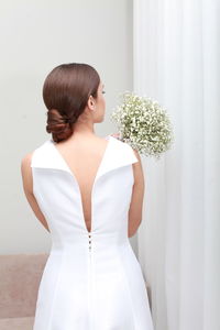 Back view of unrecognizable woman with  hairstyle in wedding dress with arms raised holding bouquet