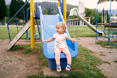 Full length of boy sitting on slide at playground