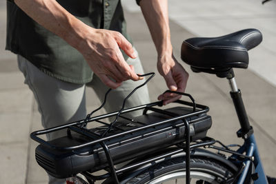 Unrecognizable crop male touching trunk of modern bike parked in city street on sunny day