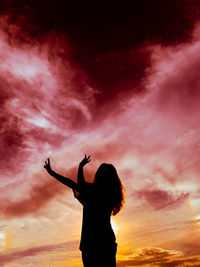 Rear view of silhouette woman standing against sky during sunset