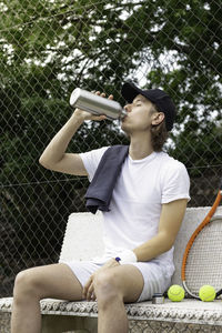 Tennis player drinking water sitting on a bench resting after playing a tennis match on a court 