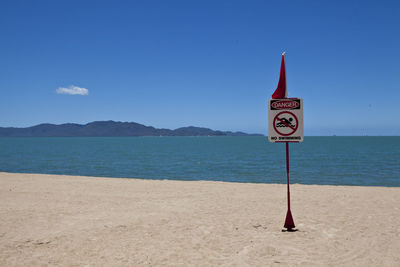 Information sign on beach against blue sky
