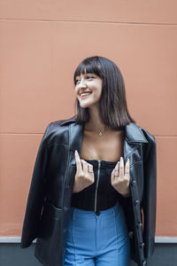 Happy young woman wearing leather jacket in front of wall