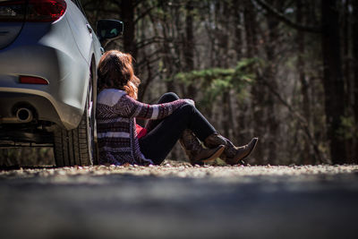 Woman sitting against car