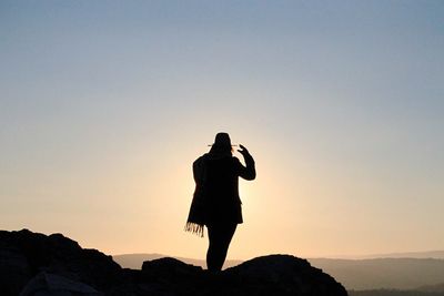 Silhouette woman standing on cliff against clear sky during sunrise