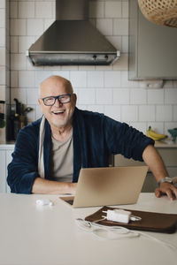 Portrait of happy senior man with laptop on kitchen island at home