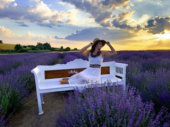 Woman with umbrella on purple flowering plants against sky during sunset