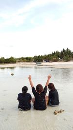 Rear view of people sitting on lakeshore against sky