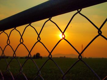 Close-up of chainlink fence on field against sky during sunset