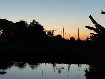 Silhouette trees by lake against sky during sunset