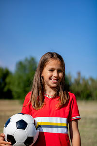 Portrait of smiling girl holding soccer ball against clear sky
