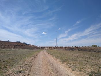 Dirt road amidst field against sky