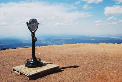 Coin-operated binoculars on cliff against cloudy sky