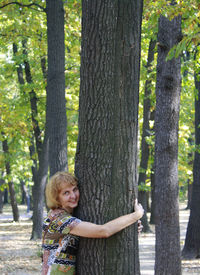 Portrait of senior woman embracing tree trunk in forest