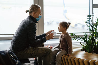 Father putting face mask on childs face at the airport. man protects girl from coronavirus at public