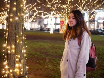 Beautiful woman standing by illuminated tree at night