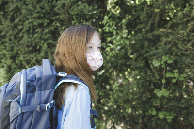 Girl wearing mask while standing with backpack