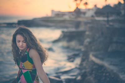 Portrait of young woman standing against sea at sunset