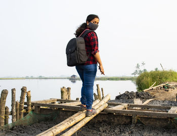 Full length of woman wearing mask standing against lake