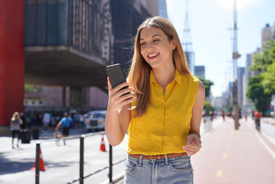 Brazilian girl using smartphone on sunny day in paulista avenue, sao paulo, brazil