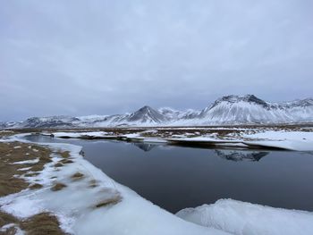 Scenic view of frozen lake by snowcapped mountains against sky