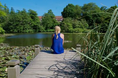 Rear view of woman standing by lake against trees