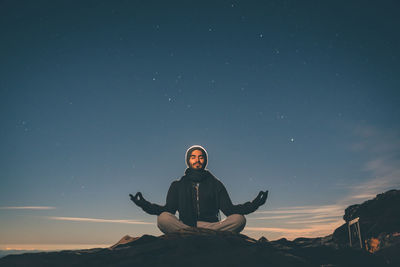 Young man meditating on mountain against sky
