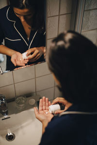 Woman reflecting in mirror while taking medicine by sink at bathroom