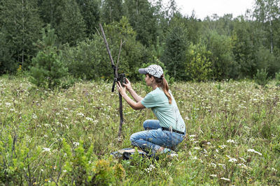 Young woman zoologist sets camera trap for observing wild animals in forest, collect scientific data