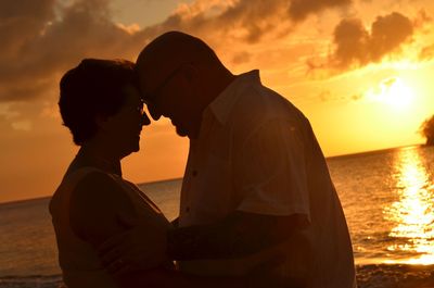 Side view of romantic couple looking at each other against sea during sunset