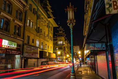 Illuminated light trails on street amidst buildings in city at night