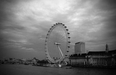 Ferris wheel in city against cloudy sky