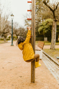 Cute girl with yellow jacket climbing in the park