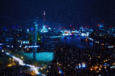 Illuminated cityscape at night seen through wet glass window during monsoon