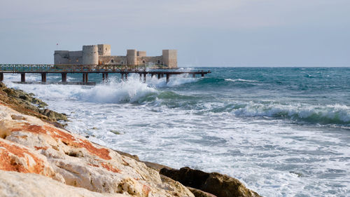 Rocky coast and pier near ancient fortress kizkalesi or maiden castle on island in mediterranean sea