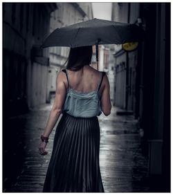 Rear view of young woman with umbrella walking on street during rainy season