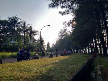 People relaxing in park by street against sky