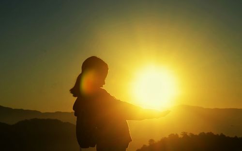 Optical illusion of silhouette woman holding sun against clear sky