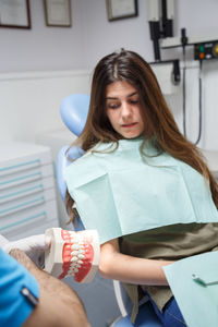 Professional doctor demonstration process of healthy teeth brushing to young woman sitting in chair.