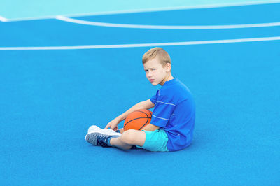 Portrait of boy sitting with basketball at court