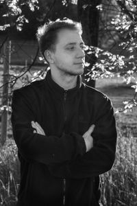 Young man looking away while standing against trees