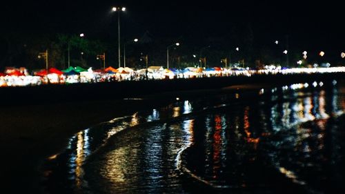 Illuminated city by river against sky at night