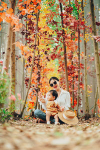Smiling mother with son sitting against autumn tree in forest