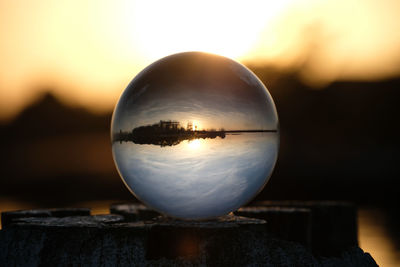 Reflection of crystal ball on glass against sky during sunset