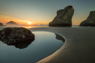 Rock formations in sea against sky during sunset